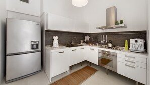 Una cocina moderna con armarios blancos, un refrigerador de acero inoxidable, un horno empotrado y una cafetera.