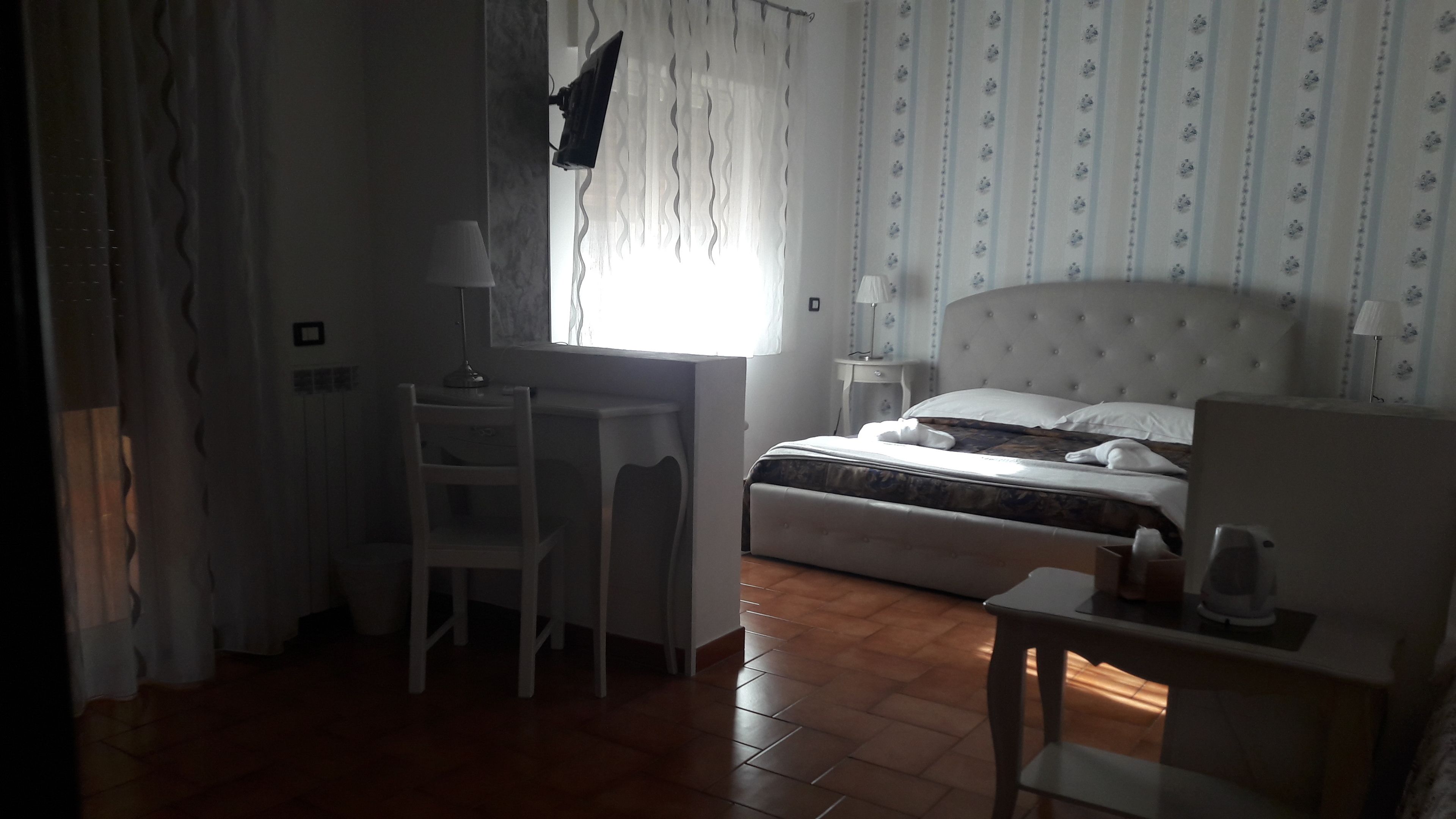 Una habitación de hotel con cama, escritorio, silla, mesita de noche y ventana con cortinas.