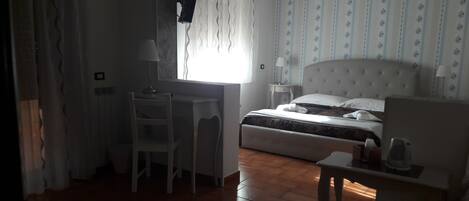 Una habitación de hotel con cama, escritorio, silla, mesita de noche y ventana con cortinas.