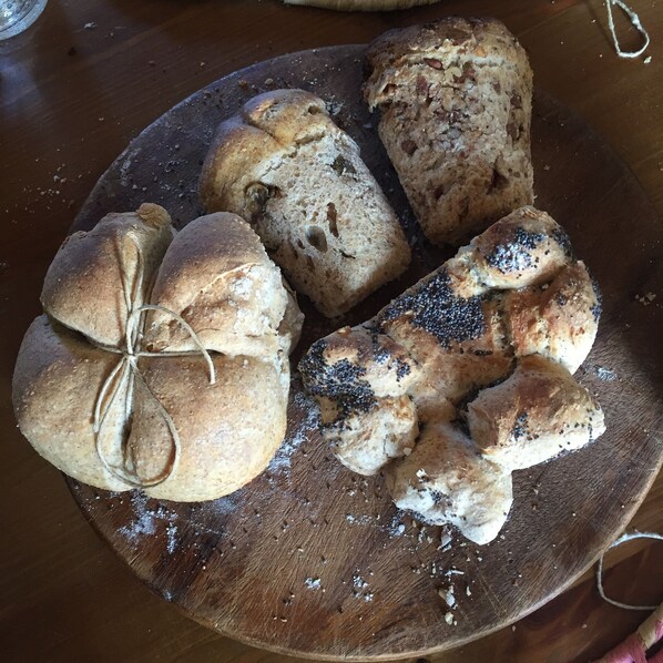 A wooden board with various types of bread, including a braided loaf and rolls with poppy seeds.