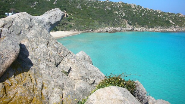 A coastal landscape with rocky terrain and a clear turquoise sea.