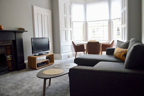 A living room with a television on a wooden stand, a sofa, a coffee table, and a fireplace.