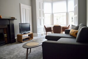 A living room with a television on a wooden stand, a sofa, a coffee table, and a fireplace. - Stylish Two Bed, Bruntsfield Apartment, Edinburgh (Edinburgh)