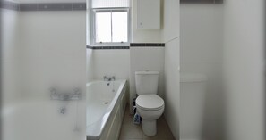A bathroom with a bathtub, toilet, and a window.