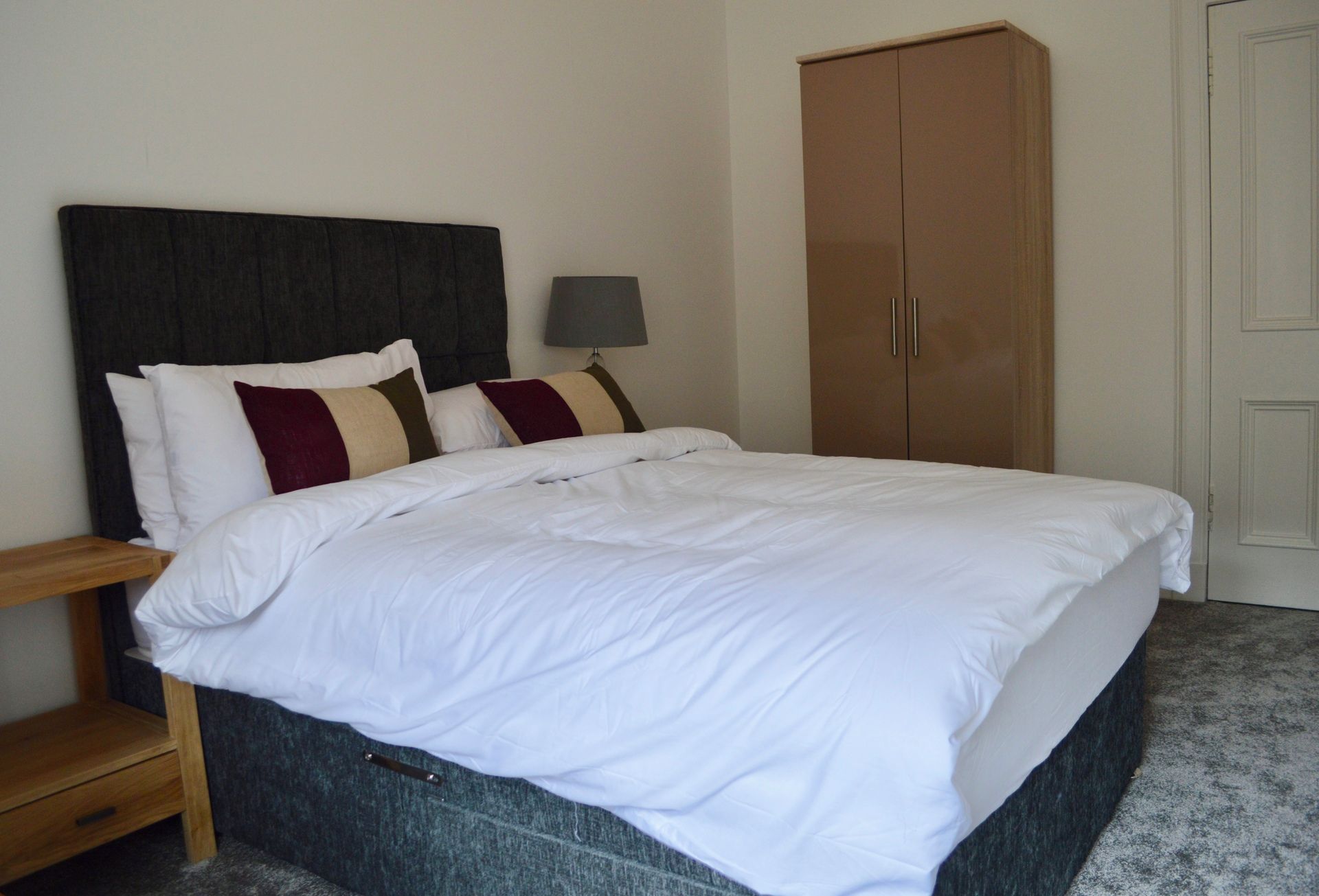 A bedroom with a bed, a wardrobe, a bedside table, and a lamp.