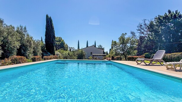 Una piscina cristalina con sillas de descanso y un edificio al fondo.