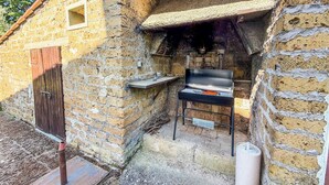 Un edificio de piedra con puerta de madera, una parrilla y un estante pequeño.