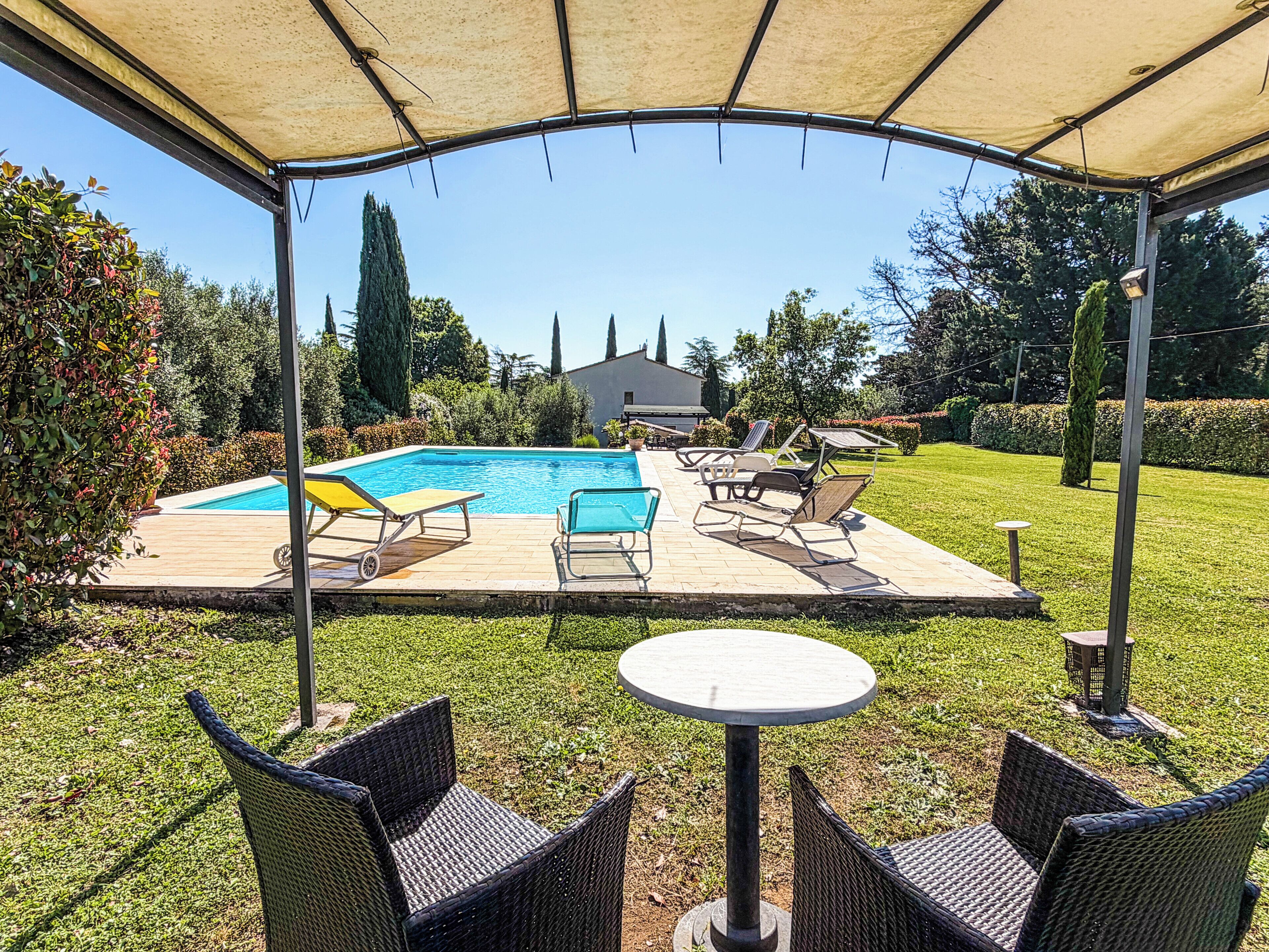 A covered outdoor area with a pool, lounge chairs, and a table.