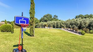 Una cancha de baloncesto con aro, rodeada de césped cuidado y árboles.