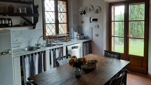 A kitchen with a wooden table, a sink, and a window with a view of greenery. - Villa Banditello, secluded, panoramic view over Montepulciano valley. (torrita di siena, fraz. montefollonico)