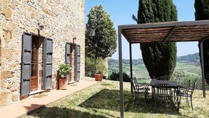 Un edificio de piedra con un patio que cuenta con una pérgola y mobiliario exterior.