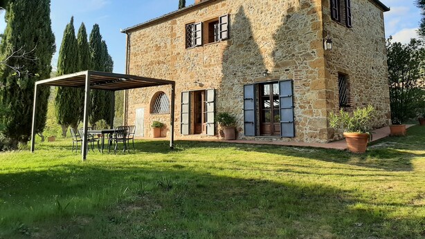 A stone house with a covered patio, potted plants, and a grassy yard. - Villa Banditello, secluded, panoramic view over Montepulciano valley. (torrita di siena, fraz. montefollonico)