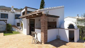 Une terrasse avec un barbecue, une chaise et un bâtiment blanc doté d’une cheminée.