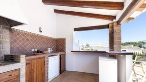 Une cuisine avec un mur de fond en briques, des meubles en bois, un lave-vaisselle blanc et un petit réfrigérateur.