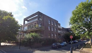 A modern multi-story residential building with balconies, a no entry sign, and parked cars along the street. - Spacious and Modern 1BD Flat w Balcony in Lambeth (London)