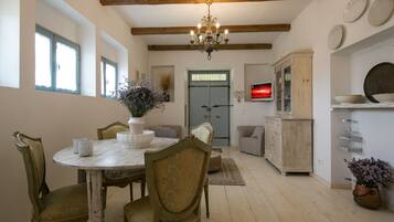 A dining area with a round table, chairs, and a chandelier. There is a cabinet and a television on the wall.
