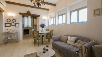 A cozy living room with a sofa, a dining table with chairs, a chandelier, and a fireplace.