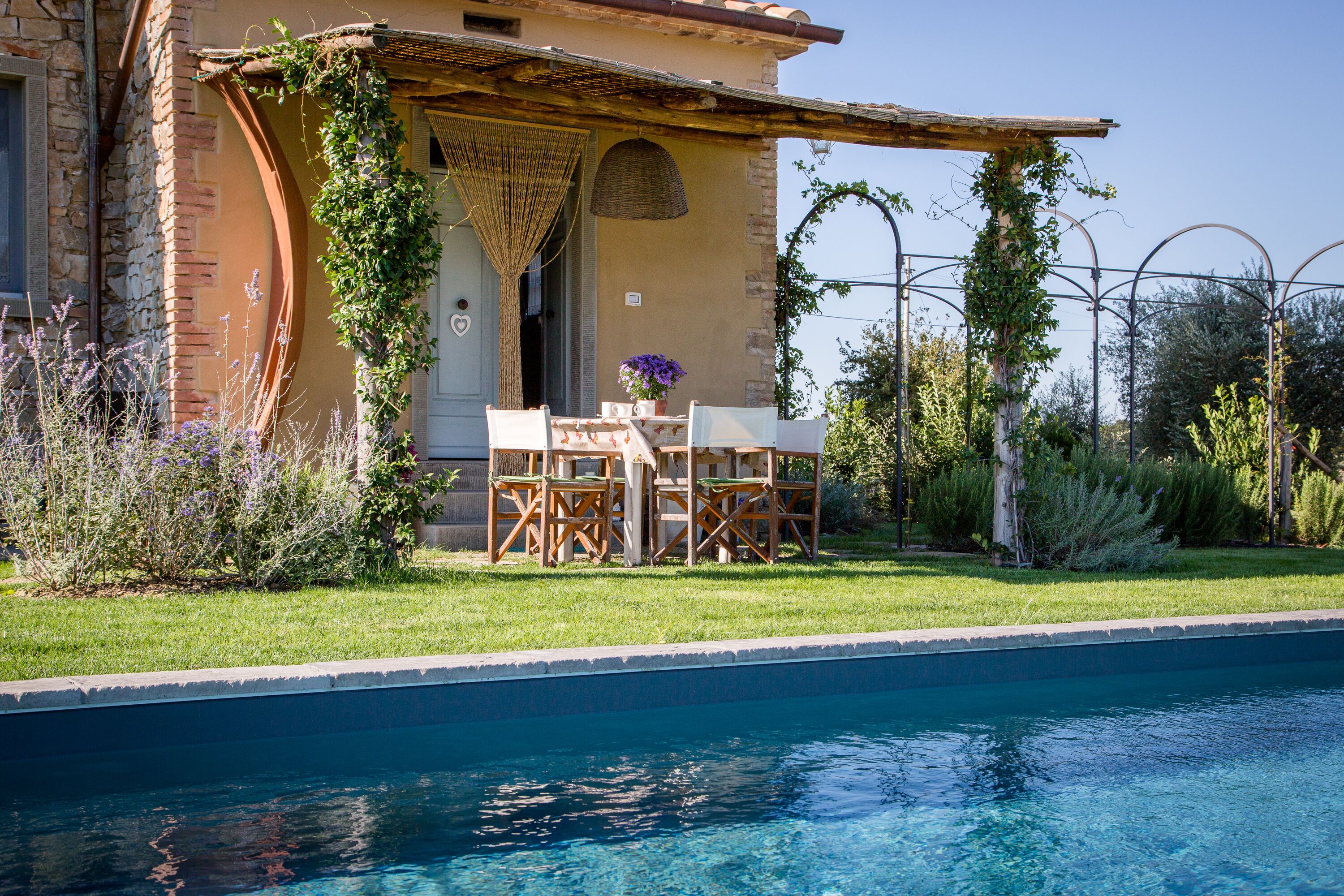 A poolside area with a pergola, outdoor seating, and a view of a pool.