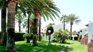 A courtyard with palm trees, a pathway, and a building with a white facade. - Cabins 59 by homeprive (Denia)