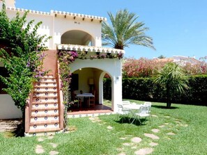 A building with a covered outdoor seating area, a staircase, and a palm tree.