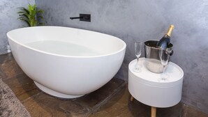 A large white bathtub, a champagne bottle in a metal bucket, and two wine glasses on a small white table. - Converted stable room 2 (York)