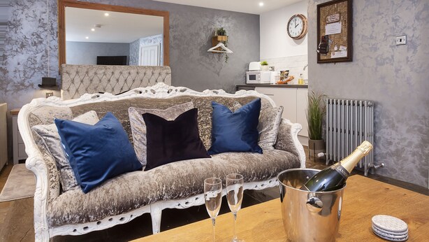 A living room with a white sofa, two blue cushions, a wooden coffee table, two champagne flutes, and a champagne bottle in a metal bucket. - Converted stable room 2 (York)