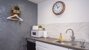 A modern kitchen with a wooden countertop, a microwave, a coffee maker, a sink with a dish rack, and a clock on the wall. - Converted stable room 2 (York)