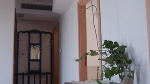 Un pasillo con techo de madera, un televisor montado en la pared, un mueble de madera con una planta y un suelo de baldosas.
