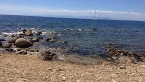 Una playa rocosa con agua cristalina y un velero a lo lejos.