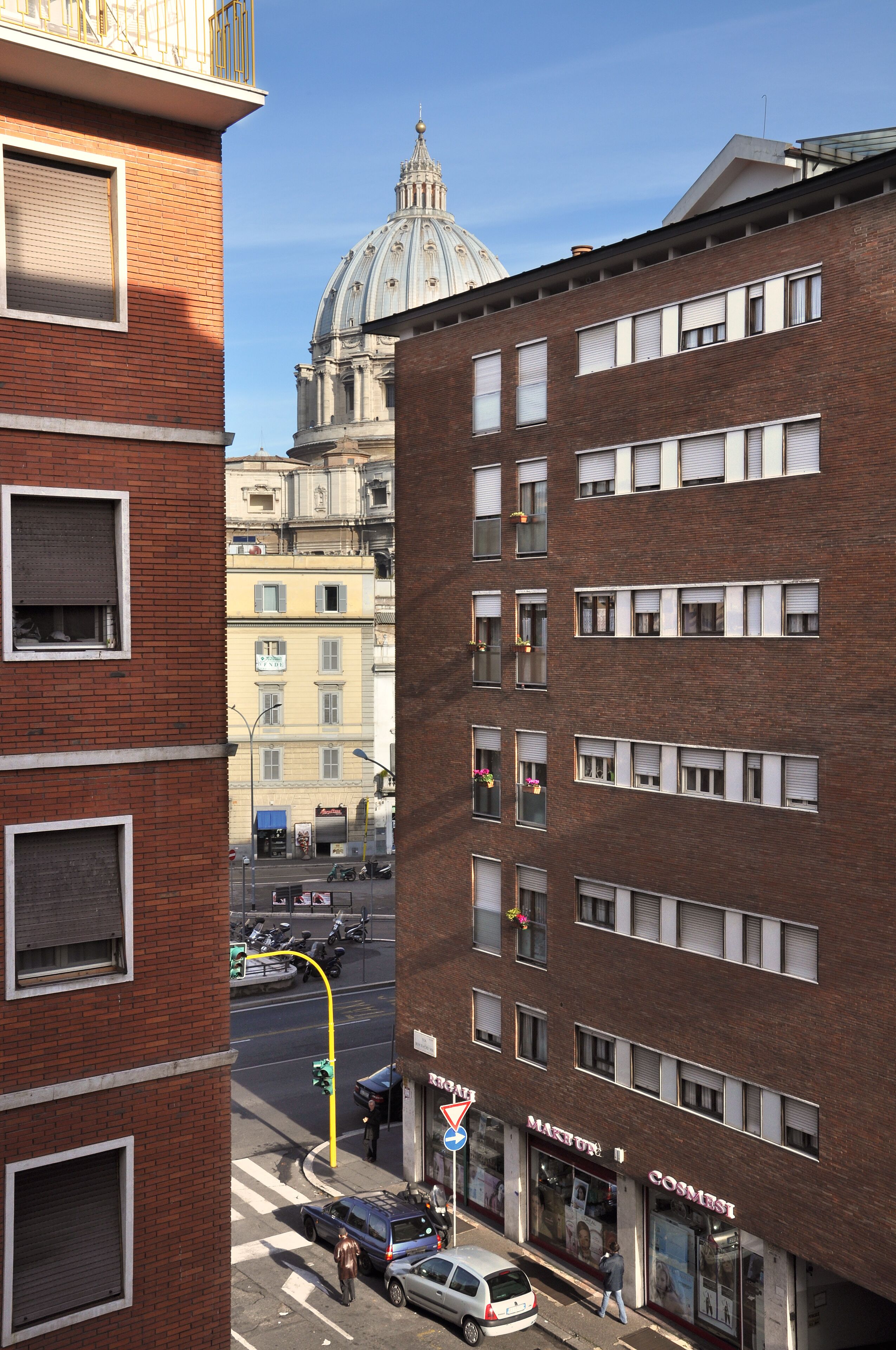 Straßenansicht mit einem markanten rotbacksteingebäude, einer Kuppel im Hintergrund und einem Laden mit einem Schild.
