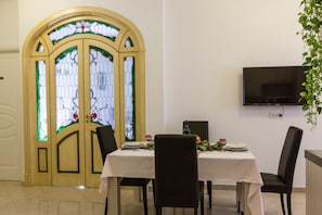 A dining area with a table set for two, a television mounted on the wall, and a stained glass door. - LOVELY APARTMENT CENTER OF ROME 100 METRES FROM ST. PETER’S BASILICA FREE WIFI (Roma)