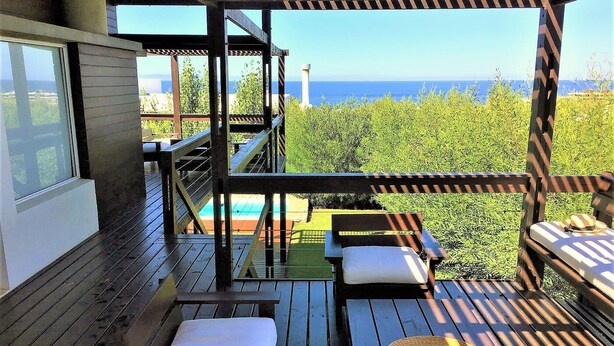 A wooden deck with outdoor seating, a pool, and a view of the ocean.