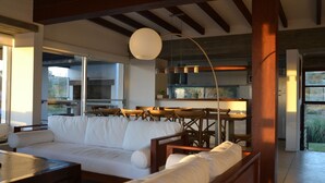 A modern living room with a white sofa, wooden chairs, a dining table, and a kitchen in the background.