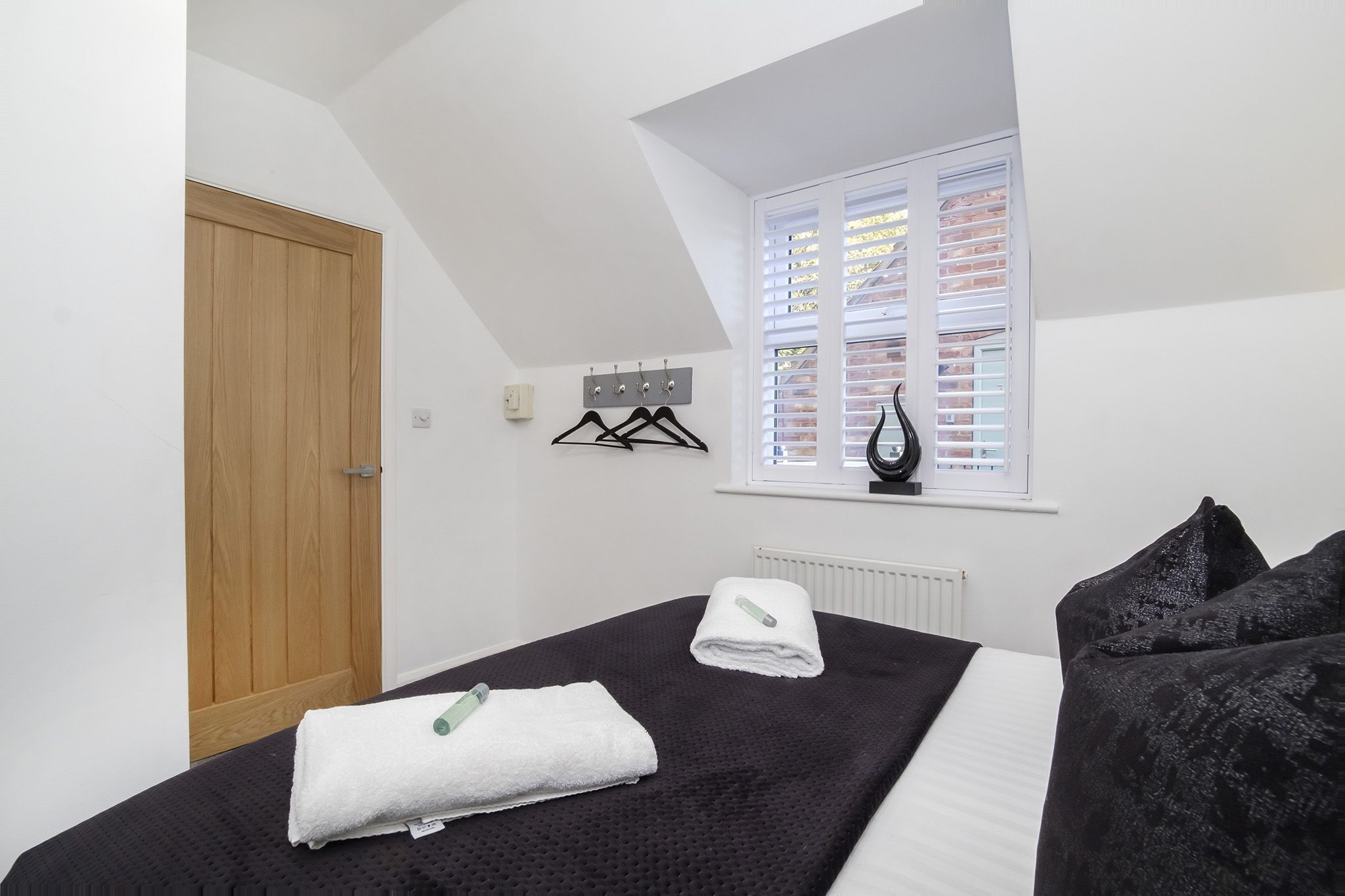 A bedroom with a bed, a window with blinds, a radiator, and a door.