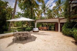 An outdoor patio with a stone floor, a round table with chairs, a white umbrella, and a wooden bench. - PIÑAS 13 Tropical Holidays in Casa de Campo - 4BDR with private pool and jacuzzi (Casa de Campo)