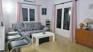 A living room with a sofa, two chairs, a coffee table, and a lamp. There are two windows with curtains, an air conditioning unit, and a picture on the wall. - villa CELINE  - Moraira (Moraira)