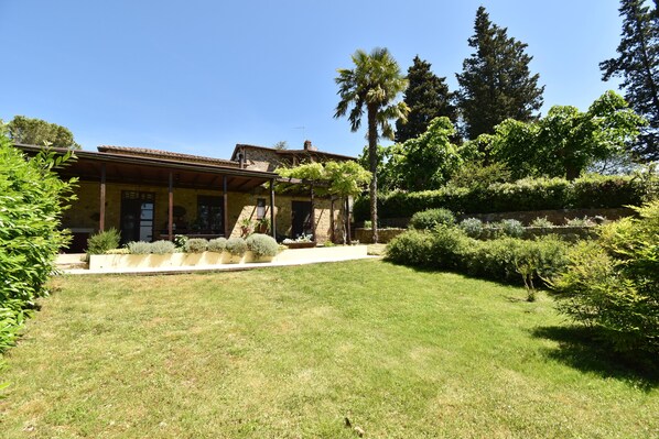 A yellow building with a tiled roof, surrounded by a well-maintained lawn and various shrubs.