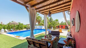 A pool area with a wooden pergola, outdoor seating, and a dining table with a vase of flowers. - Villa Felisa Holiday Home, Seville Countryside. (La Puebla de Cazalla)