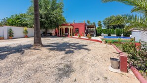 A courtyard with a pool, palm trees, and a red building with arches. - Villa Felisa Holiday Home, Seville Countryside. (La Puebla de Cazalla)