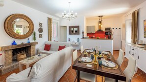 A modern living room with a fireplace, a dining table set for four, and a kitchen in the background. - Villa Felisa Holiday Home, Seville Countryside. (La Puebla de Cazalla)