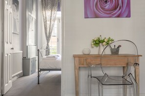 Ein Hotelzimmer mit einem Bett, einem Holztisch, einem Stuhl, einer Vase mit Blumen und einem Wandbild.