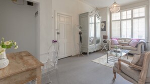 Ein geräumiges Wohnzimmer mit weißer Tür, einem Glastisch, einem weißen Sofa und einer Deckenleuchte.