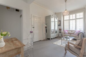 Ein geräumiges Wohnzimmer mit weißer Tür, einem Glastisch, einem weißen Sofa und einer Deckenleuchte.