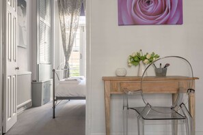 Ein Schlafzimmer mit einem Bett, einem Holztisch mit Stuhl, einer Vase mit Blumen und einem Bild an der Wand.