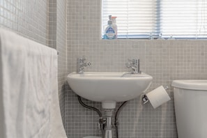 Ein Badezimmer mit einem weißen Waschbecken, einer Toilette und einem Fenster mit Jalousien.