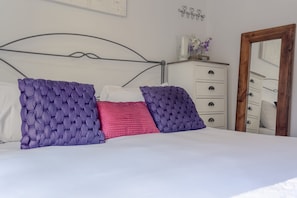 Ein Bett mit Metallkopfteil, eine weiße Kommode mit Schubladen und ein Spiegel mit Holzrahmen.