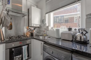 Eine moderne Küche mit Edelstahlgeräten, einem eingebauten Ofen, einer Waschmaschine und einem großen Fenster mit Blick auf die Stadt.