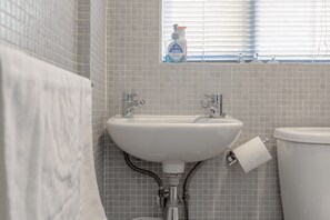 Ein Badezimmer mit einem weißen Waschbecken, einer Toilette und einem Fenster mit Jalousien.