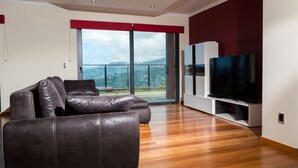 Una sala de estar moderna con un sofá de cuero, un televisor de pantalla plana y un gran ventanal corredera que da a un balcón con vistas a la ciudad.