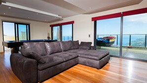 Una sala de estar moderna con un sofá seccional, una mesa de billar y vistas al mar a través de amplios ventanales.